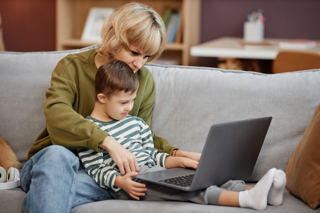 Mother and son using a laptop together while sitting on a sofa at home.