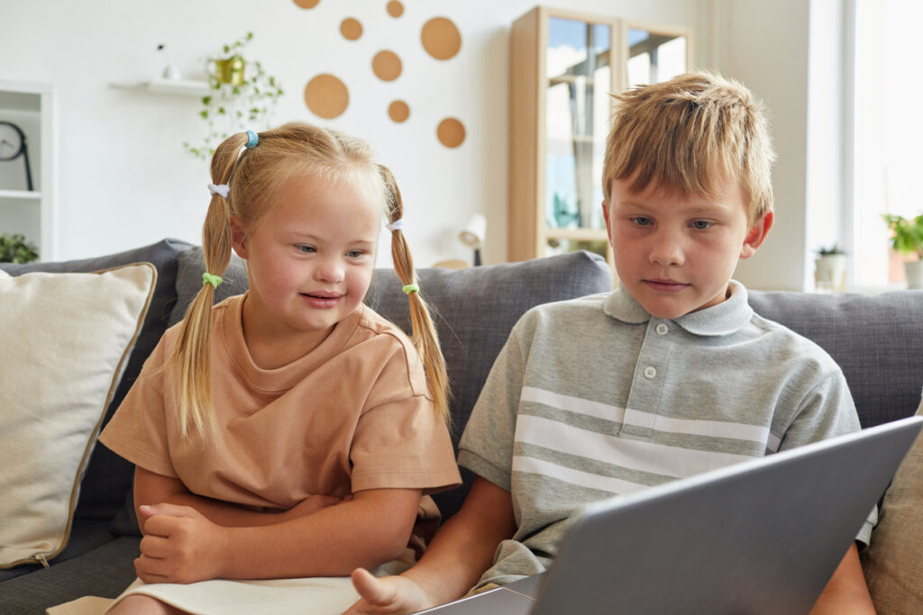 AI for autism: Children using a laptop while sitting on a sofa at home.